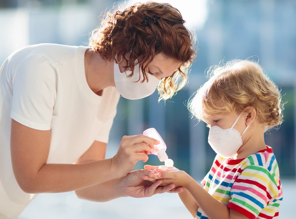 Mother and child wearing face masks while washing their hands with sanitiser