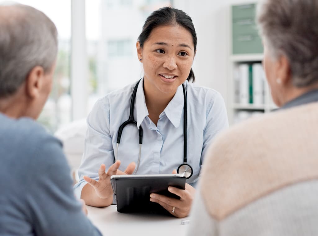 Female general practitioner holding a digital device and talking to two elderly patients.