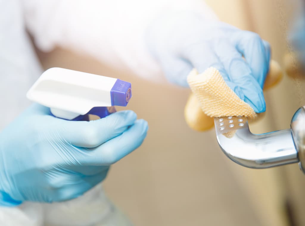 Hands with blue gloves holding a spray bottle, cleaning a door handle